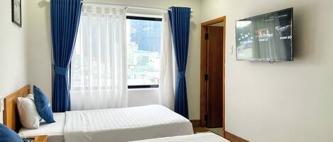 Une chambre d’hôtel avec deux lits, un téléviseur fixé au mur et une fenêtre avec des rideaux.
