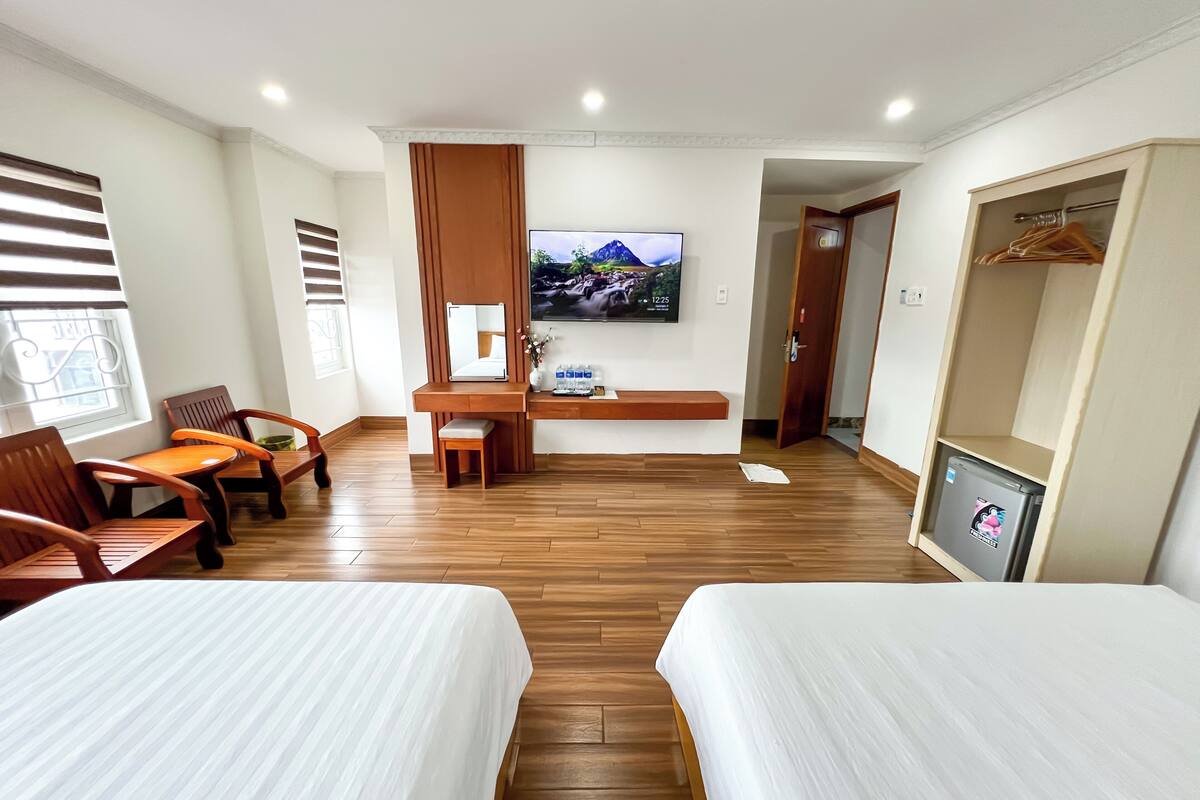 A hotel room with two beds, a desk with a chair, a TV, and a wardrobe.