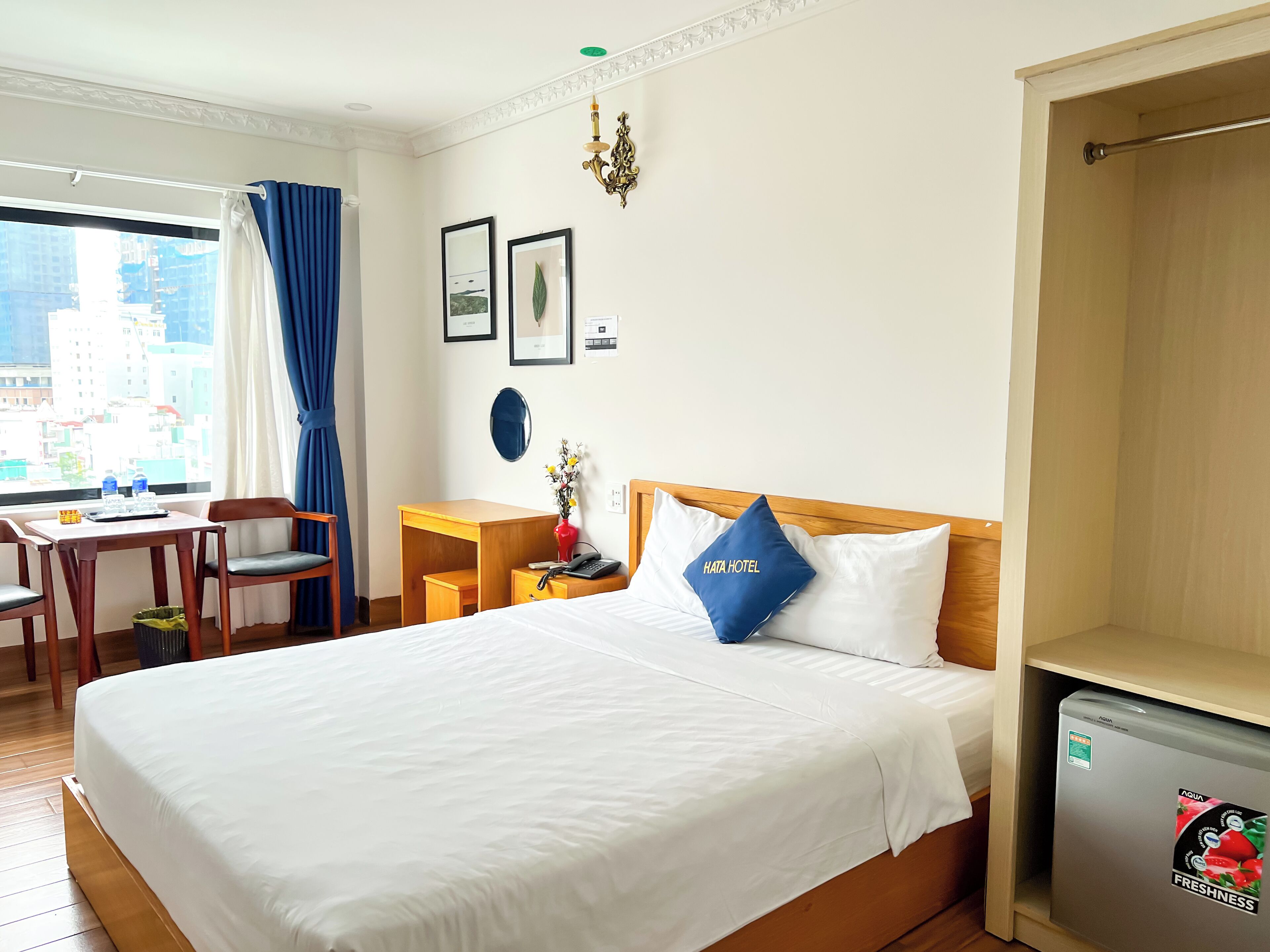 A hotel room with a bed, a desk, a chair, a small refrigerator, and a window with curtains.