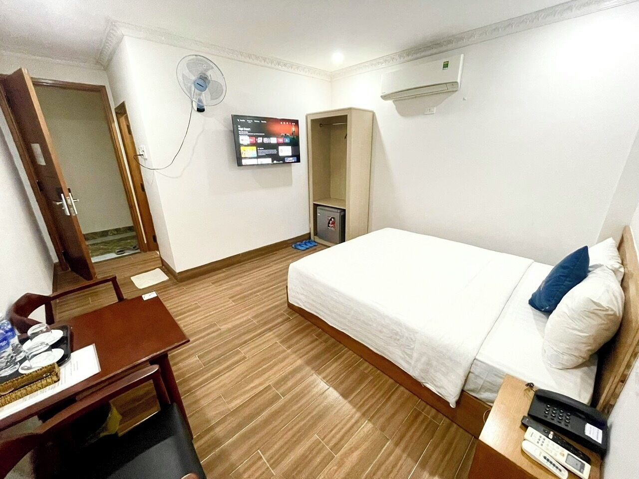 Een hotelkamer met een bed, een bureau met stoel, een aan de muur bevestigde televisie en een airconditioner.