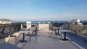 A terrace with tables and chairs, overlooking a coastal view with buildings and a flag. - Hata hotel (Quy Nhon Nam)