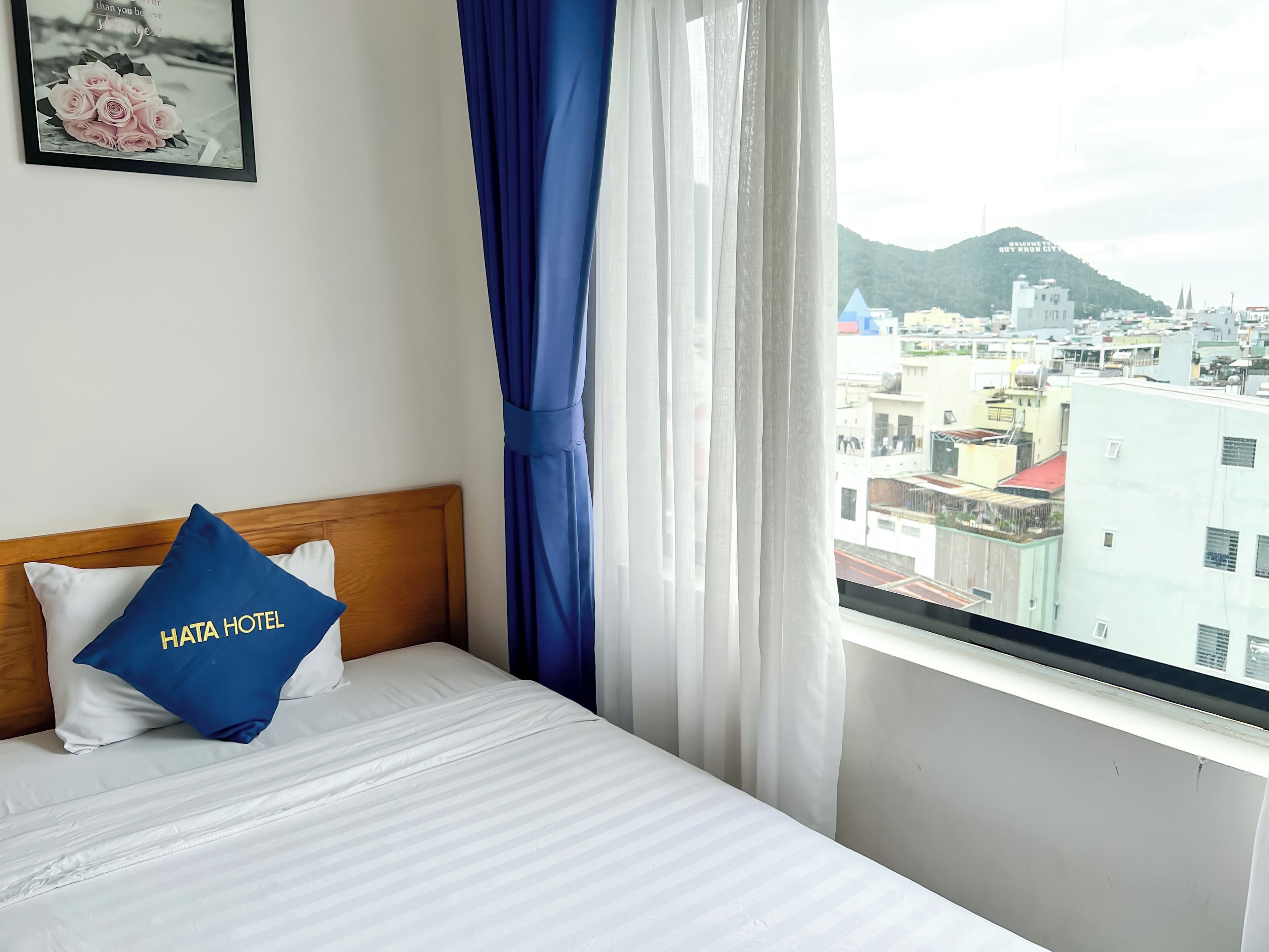 Quarto de hotel com cama, travesseiro com a inscrição "HAITA HOTEL", quadro na parede e vista da cidade pela janela.