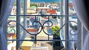 A view from a window with white curtains, overlooking a coastal cityscape with buildings and a clear blue sky. - Hata hotel (Quy Nhon Nam)