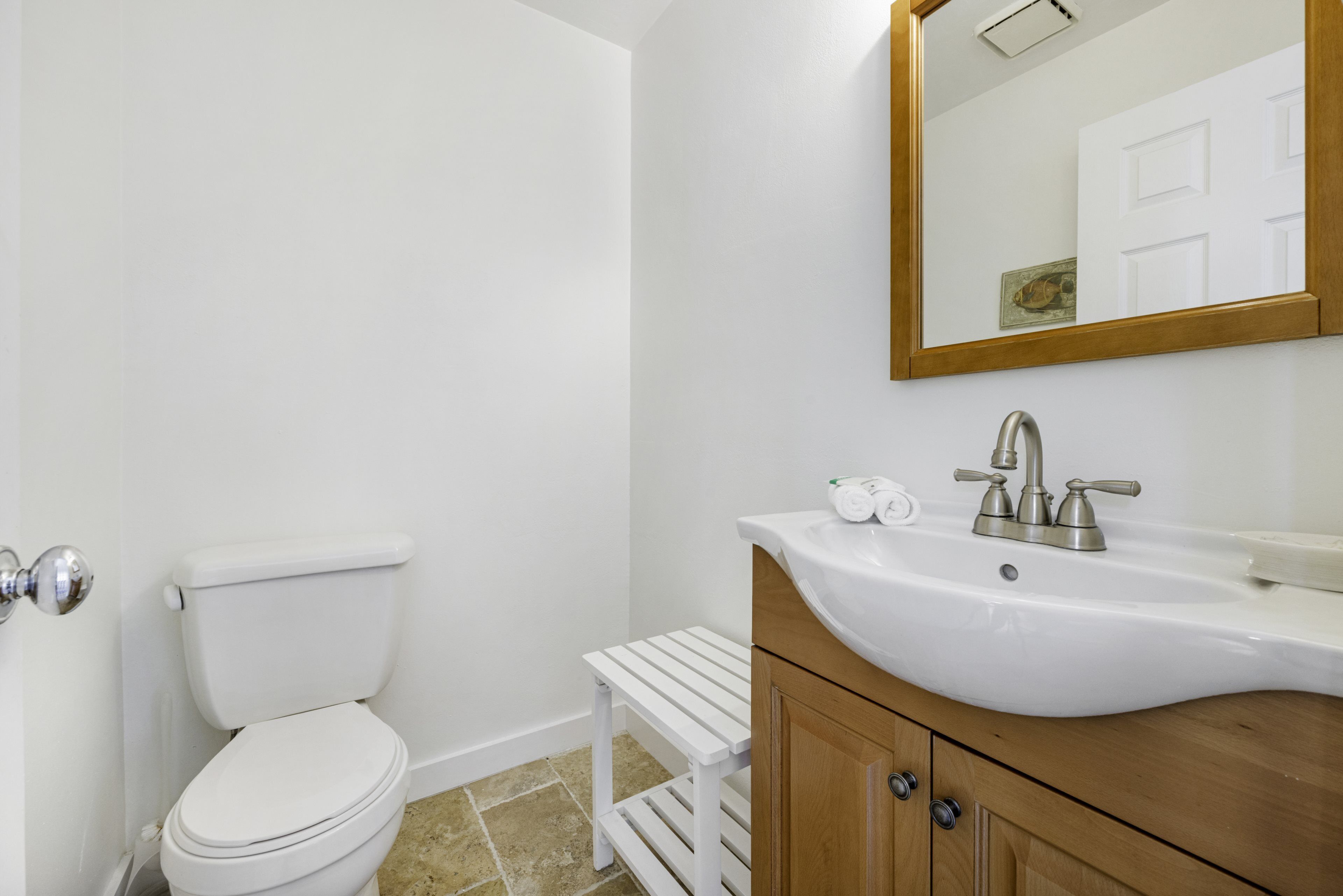Un baño con inodoro blanco, un lavabo blanco con tocador de madera y un espejo sobre el lavabo.