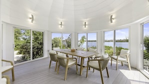 Una habitación amplia con una gran mesa y sillas de madera, ventanas grandes con vista al lago e iluminación empotrada en el techo.