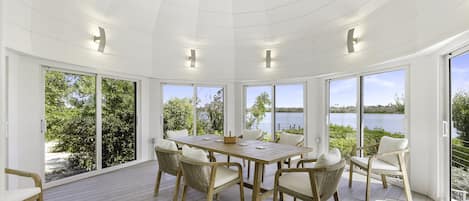 A spacious room with a large wooden table and chairs, large windows with a view of the lake, and a ceiling with recessed lighting.