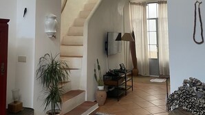 Ein geräumiger Wohnbereich mit einer Treppe, die zu einer oberen Etage führt, einem an der Wand befestigten Flachbildfernseher und einem Blumentopf in der Nähe der Treppe.