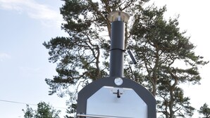 Ein tragbarer Grill für den Außenbereich mit digitalem Thermometer, platziert auf einer Holzterrasse mit Blumentöpfen.