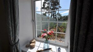 Ein Fenster mit Blick auf einen Garten, eine Vase mit Blumen und ein kleiner Tisch mit Pinsel und Behälter.