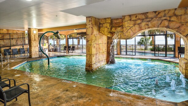 An indoor pool with a stone archway, lounge chairs, and a view of the outdoors.