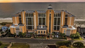 A large, multi-story hotel with a central tower, located near a beach with a view of the ocean.