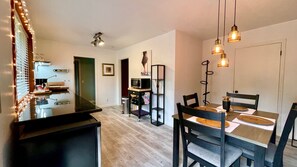 Une cuisine moderne avec un plan de travail noir, un four à micro-ondes et un évier. On y trouve également un coin repas avec une table et des chaises en bois, ainsi qu’une bibliothèque noire.