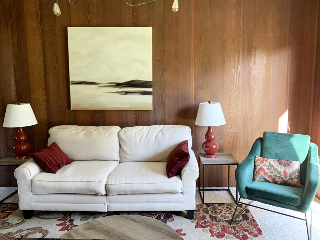 A room with a white sofa, a teal armchair, and two lamps on side tables.
