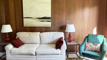 A room with a white sofa, a teal armchair, and two lamps on side tables.