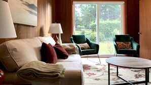 Una habitación acogedora con un sofá, dos sillones, una mesa redonda de centro y un gran ventanal con vistas a zonas verdes.
