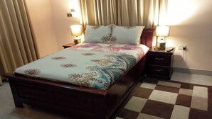Una cama con colcha estampada, dos mesitas de noche con lámparas y una alfombra a cuadros.