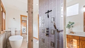 Un baño moderno con una bañera independiente, ducha con múltiples cabezales y un mueble de tocador de madera con cajones.