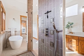 A modern bathroom with a freestanding bathtub, a shower with multiple heads, and a wooden vanity with drawers.