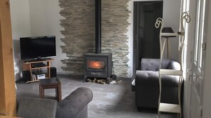 A living room with a stone wall, a fireplace, a sofa, a television, and a small table. - Gîte 4p Tout confort bord de cher, calme, Animaux ok, Zoo Beauval chenonceau (Bléré)