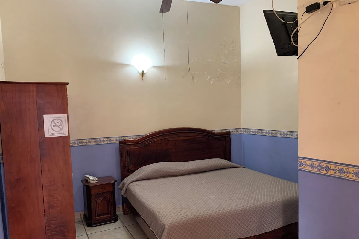 Ein Schlafzimmer mit einem hölzernen Bett, einem Nachttisch, einem Kleiderschrank und einer Wandleuchte.