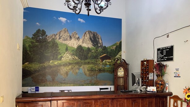 A reception desk with a large scenic mural, a wooden clock, and a sign listing room rates. - OYO Hotel Real De Cortés (Xalapa)