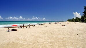 Una amplia playa de arena con cielo azul despejado y mar.