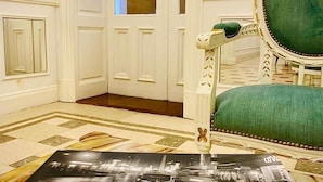 Un hall d’hôtel avec un fauteuil recouvert d’un tissu vert, un miroir de style vintage et une affiche de Buenos Aires.