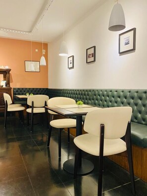 A restaurant with a green upholstered booth seating, white chairs, and a wooden table. - Hotel Chemin (Buenos Aires)