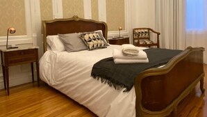 Une chambre à coucher avec un lit en bois, du linge de lit blanc, une table de chevet et une chaise.
