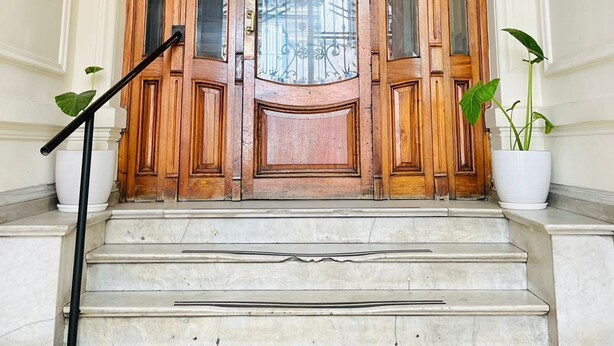 Une grande porte en bois, dotée de panneaux de verre et surmontée d’une rambarde en métal.