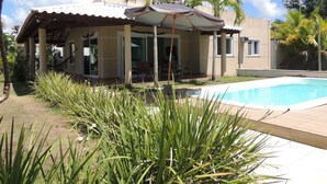Uma casa com piscina, varanda coberta e plantas tropicais.