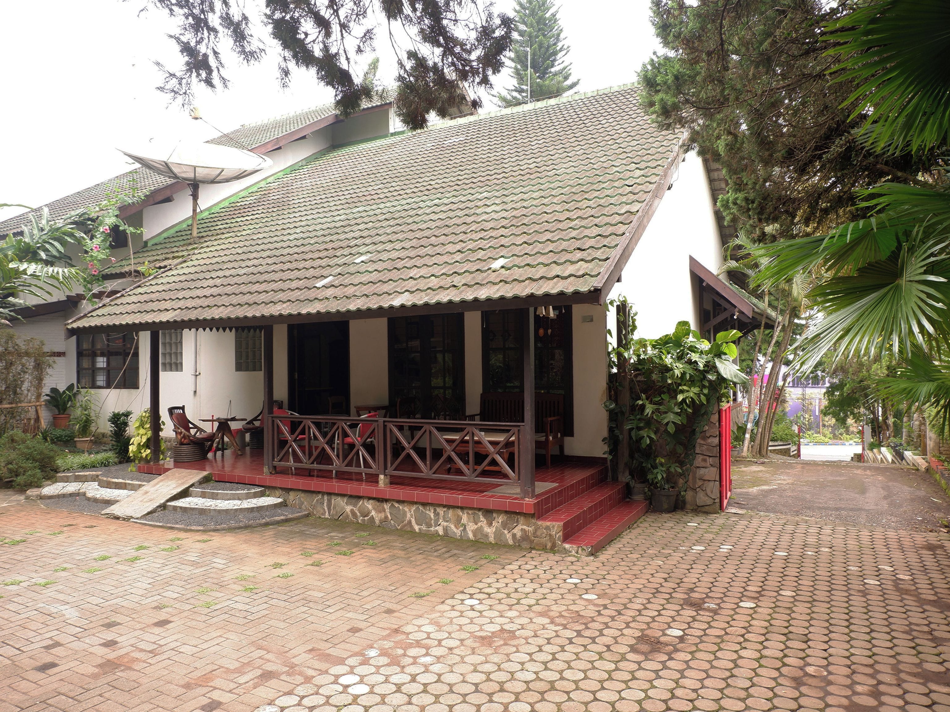 A building with a tiled roof, a covered porch with seating, and a paved entrance area.
