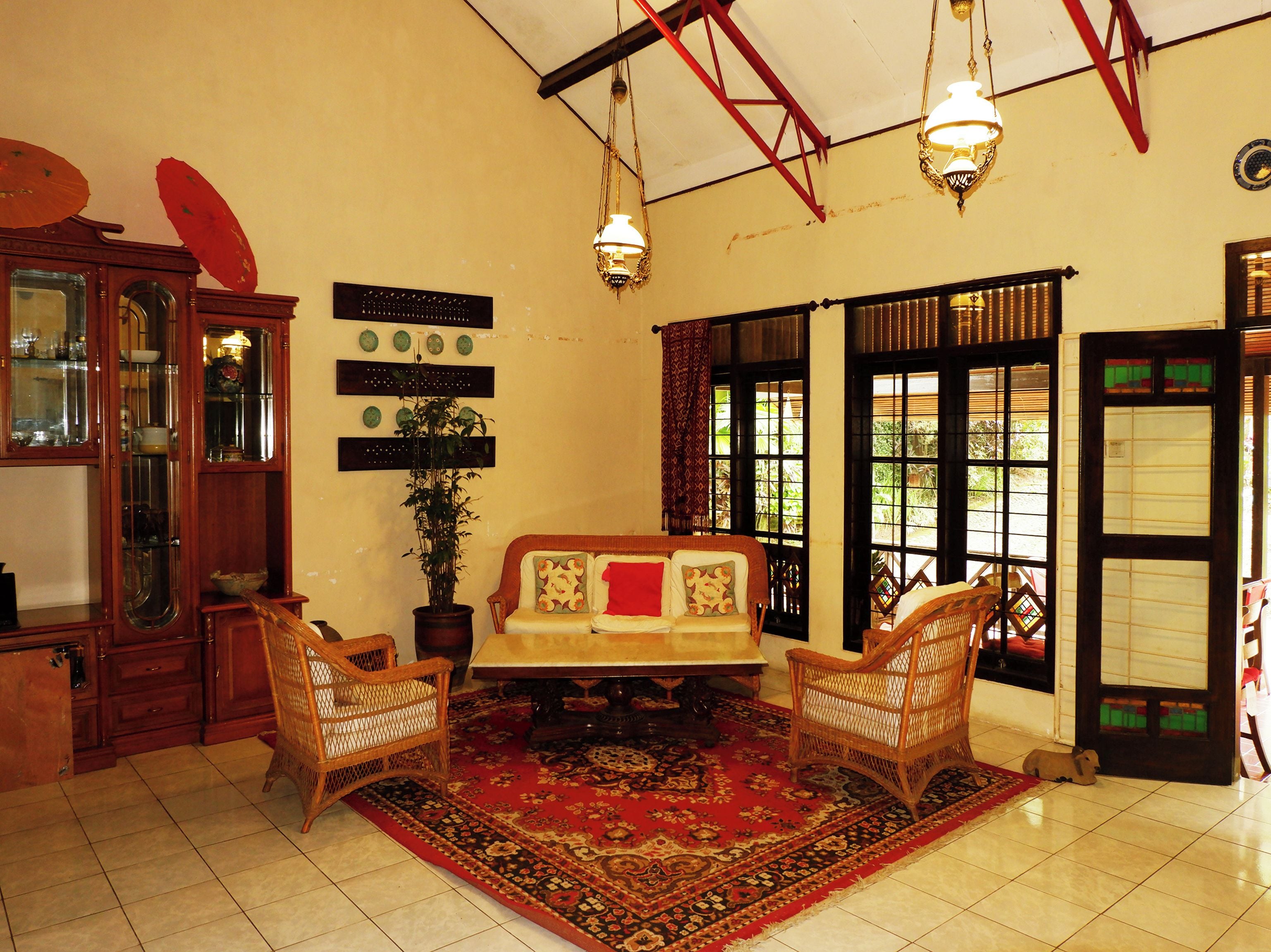 A traditional room with a sofa, two wicker chairs, a red patterned rug, a wooden cabinet, and a potted plant.