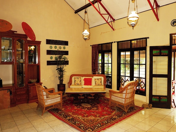 A traditional room with a sofa, two wicker chairs, a red patterned rug, a wooden cabinet, and a potted plant. - OYO 604 Cemara S Homestay (Batu)