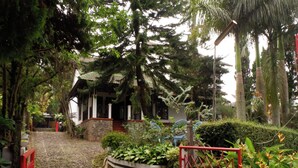 Un sentier menant à une maison traditionnelle, dotée d’un mur en pierre et d’un portail rouge.