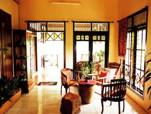A room with a tiled floor, wooden furniture, a large plant, and a view through a window with a patterned curtain. - OYO 604 Cemara S Homestay (Batu)