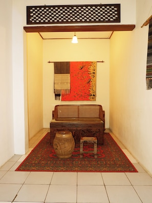 A traditional room with a wooden sofa, a patterned rug, a small stool, and a decorative vase. - OYO 604 Cemara S Homestay (Batu)