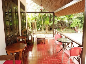 A covered outdoor seating area with wooden furniture and a view of tropical vegetation. - OYO 604 Cemara S Homestay (Batu)