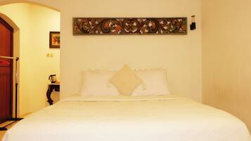 A neatly made bed with white bedding in a room with a wooden door and a decorative wall piece above it.