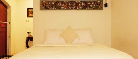 A neatly made bed with white bedding in a room with a wooden door and a decorative wall piece above it.