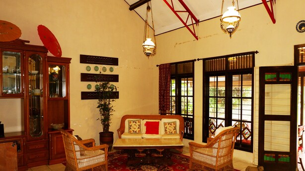 A traditional room with a sofa, two wicker chairs, a red patterned rug, a wooden cabinet, and a potted plant. - OYO 604 Cemara S Homestay (Batu)