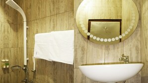 Une salle de bain avec un mur en bois, un miroir rond avec un cadre doré, un lavabo blanc et une douche avec une serviette blanche.