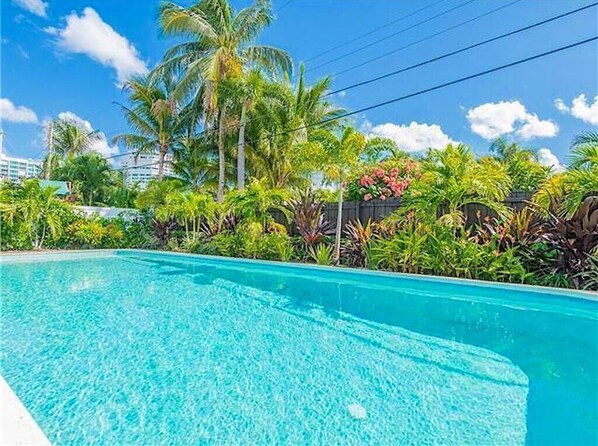 A clear swimming pool surrounded by lush greenery and palm trees.