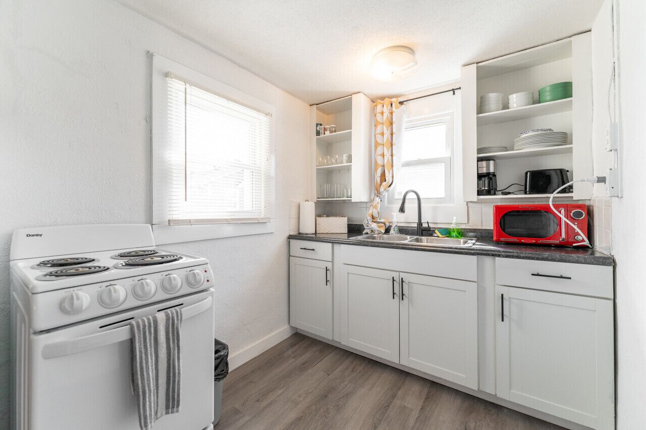 A kitchen with white cabinets, a stove, a sink, and a microwave.