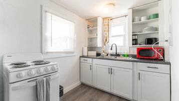 A kitchen with white cabinets, a stove, a sink, and a microwave.