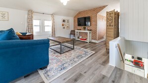Un salon moderne avec un canapé bleu, une table basse et un téléviseur fixé au mur en briques.
