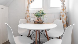 Une petite table ronde, quatre chaises blanches, un vase de fleurs et un panier rempli de livres et de bouteilles.