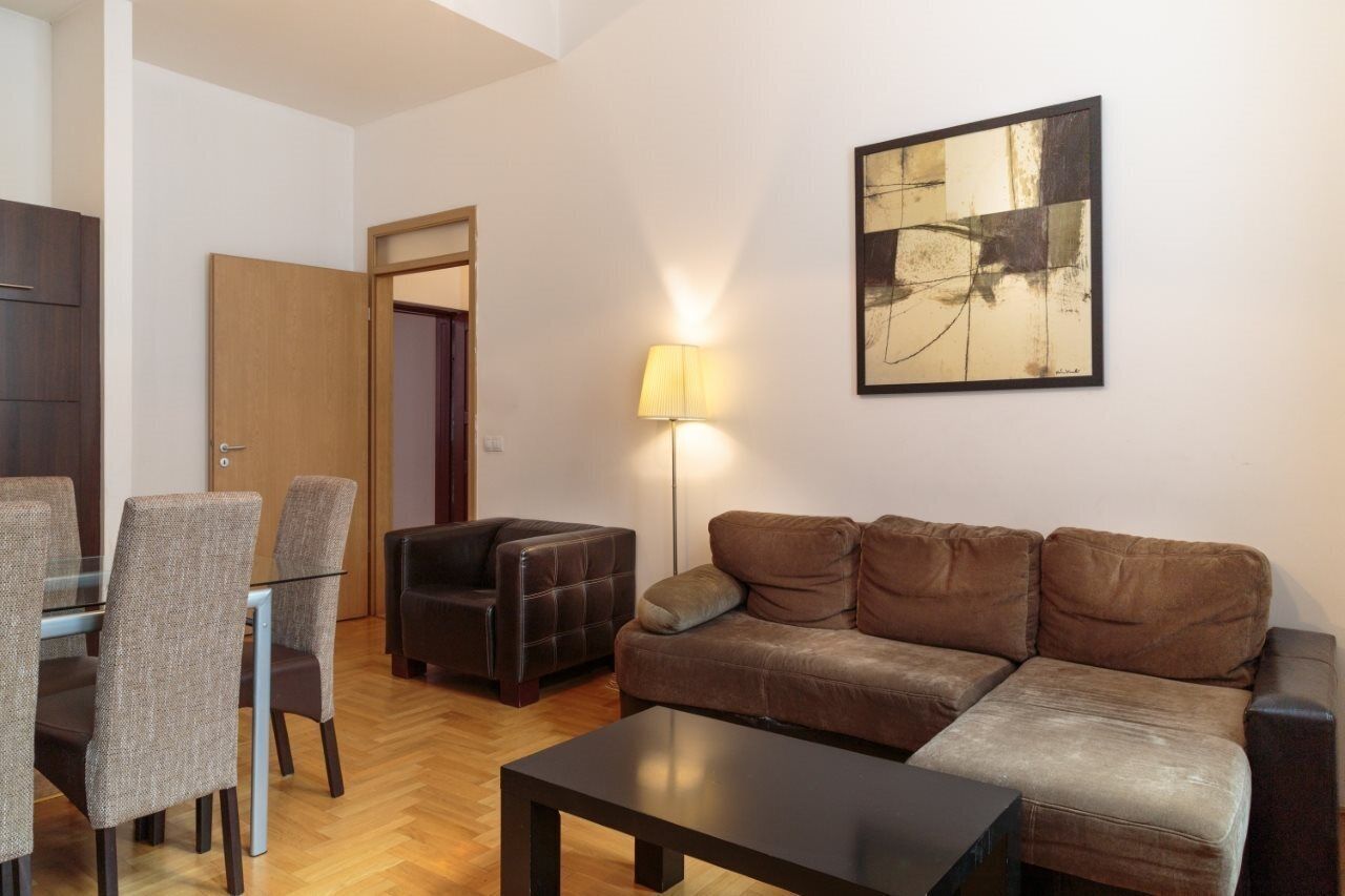 A modern living room with a brown leather sofa, a glass coffee table, and a dining area with a glass table and chairs.
