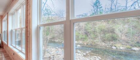 A room with large windows overlooking a river and trees.