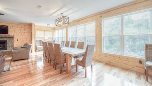 A spacious room with a wooden dining table and chairs, a fireplace, and large windows offering a view of the outdoors.